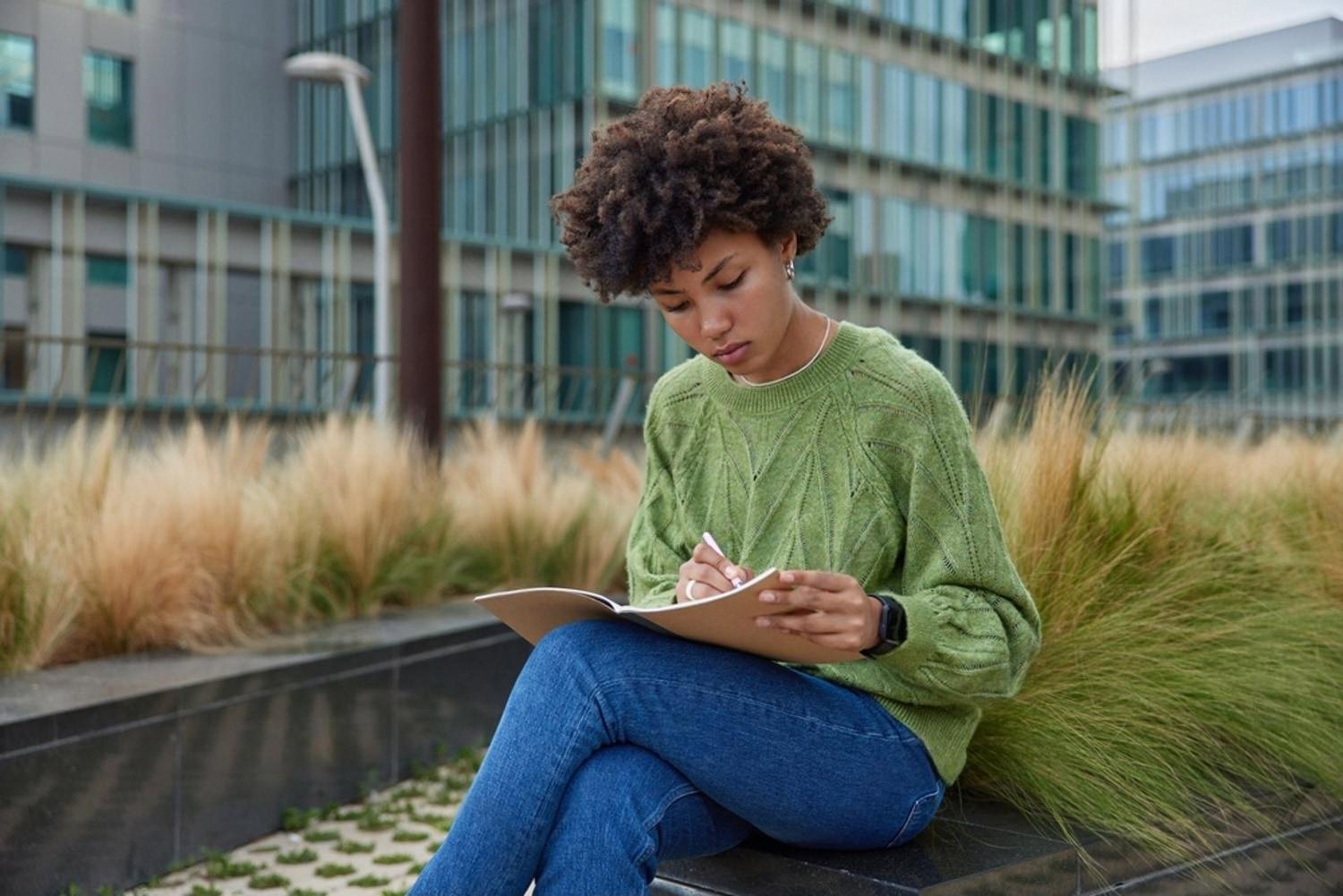 Young woman outdoors writing down her study goals near a modern UAE campus